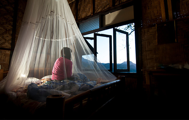 Ein Mädchen sitzt in seinem Zimmer auf einem Bett unter einem weißen Mückennetz