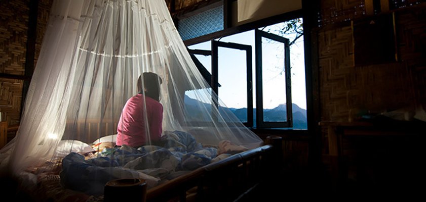 Ein Mädchen sitzt in seinem Zimmer auf einem Bett unter einem weißen Mückennetz